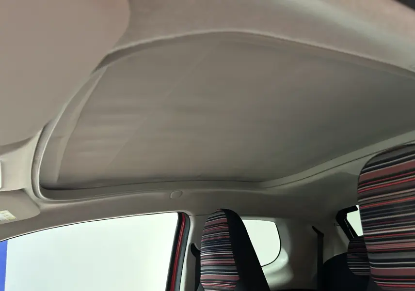 Toit ouvrant fermé vu de l'intérieur côté conducteur de la Citroën C1 rouge avec sièges rayés multicolores.