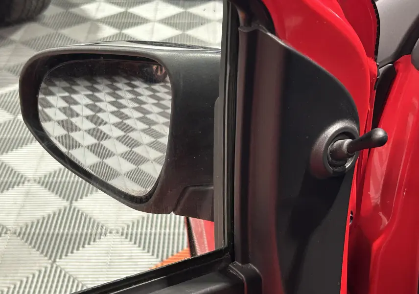 Gros plan sur le rétroviseur extérieur côté gauche d'une Citroën C1 rouge, avec poignée de réglage manuel visible.