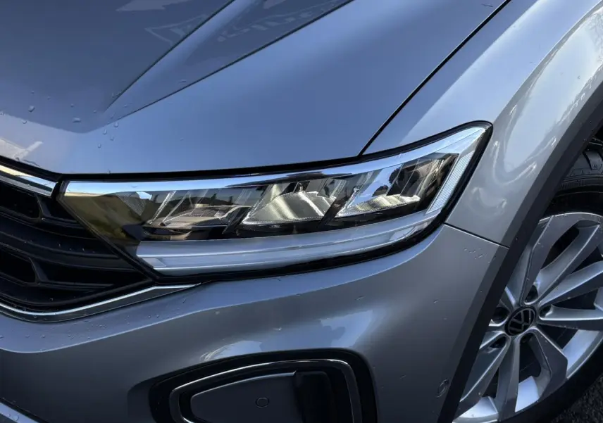 Gros plan sur l'avant droit argent pyrite du Volkswagen T-Roc 1.5 TSI 150 DSG avec phare LED et jante alliage.