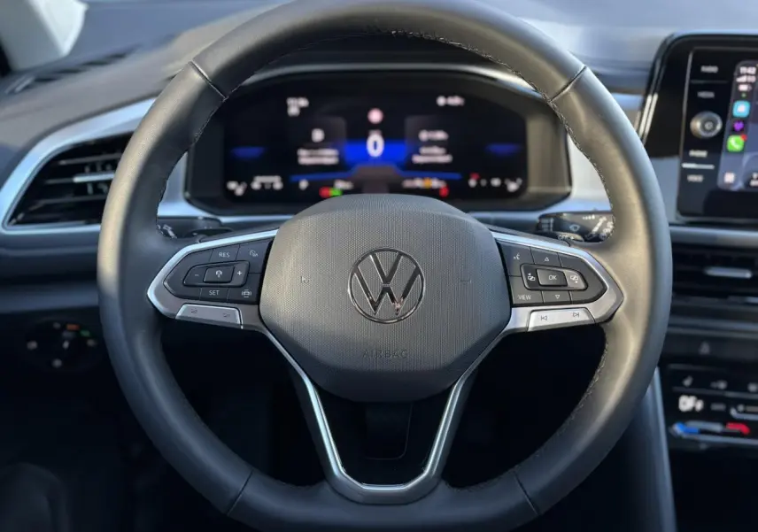 Vue rapprochée du volant en cuir multifonction noir du Volkswagen T-Roc 2025 avec tableau de bord digital en arrière-plan.