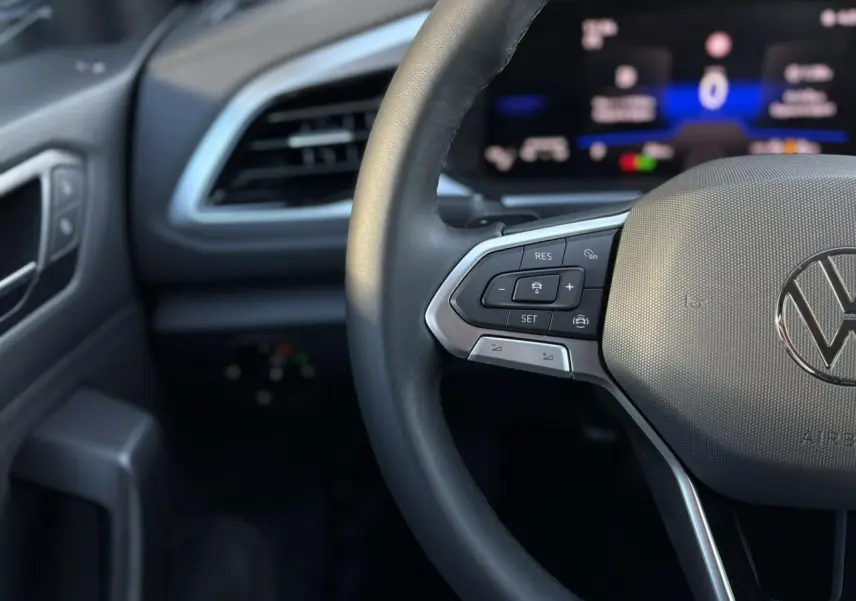 Gros plan sur le volant cuir multifonction du Volkswagen T-Roc 1.5 TSI argent avec tableau de bord digital flou en arrière-plan.