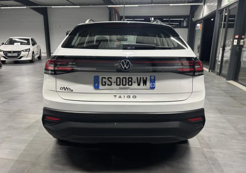 Vue arrière d'un Volkswagen Taigo blanc 2023 en intérieur avec feux arrière reliés par une bande noire brillante.