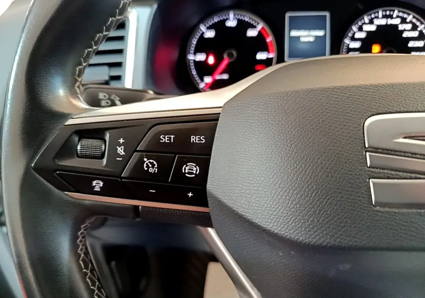 Gros plan sur le volant cuir et alu côté gauche du SEAT Ateca gris clair avec commandes multifonctions et tableau de bord lumineux.