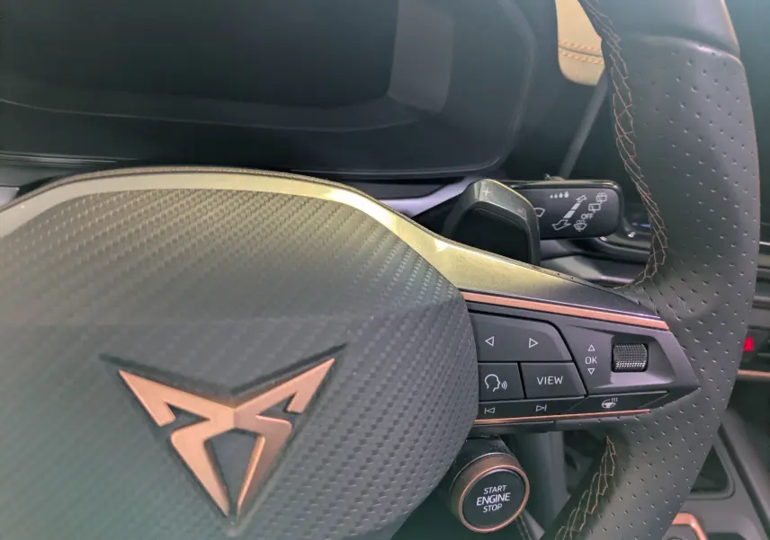 Gros plan sur le volant perforé noir avec logo CUPRA cuivré et commandes multifonctions côté droit, bouton démarrage visible.