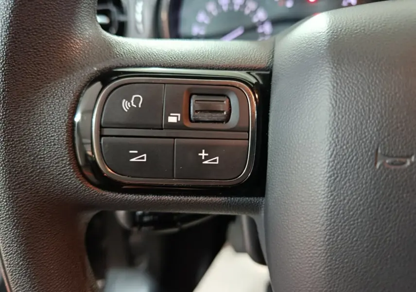 Gros plan sur les commandes multifonctions noires du volant de la Citroën C3 2024, intérieur gris foncé.