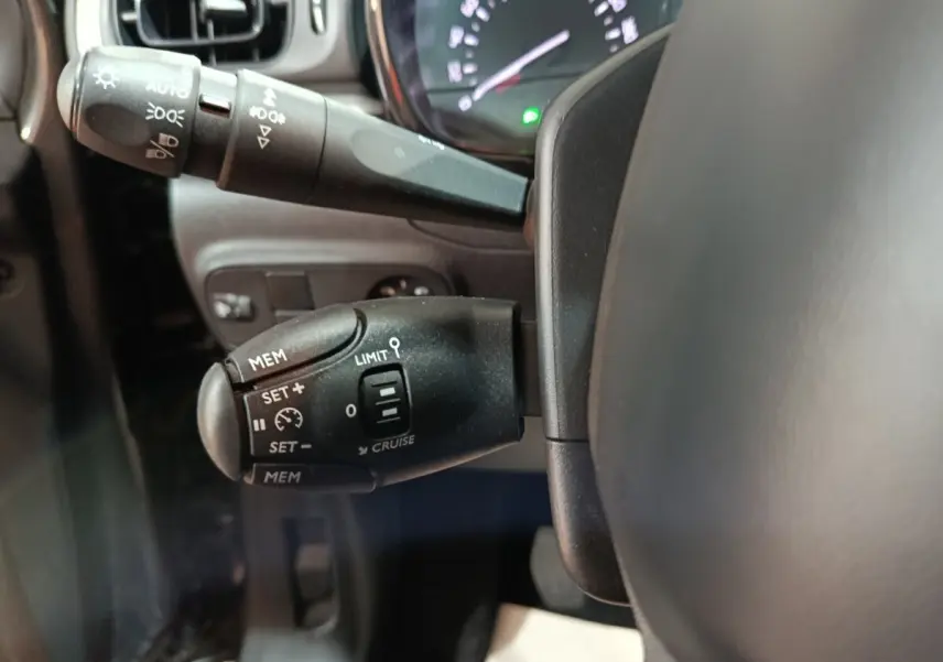 Gros plan sur la commande de régulateur de vitesse à gauche du volant dans l’habitacle d’une Citroën C3 gris foncé 2024.