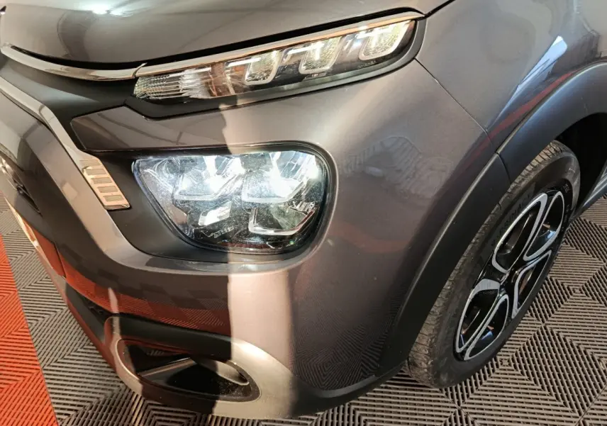 Gros plan sur l'avant droit gris foncé du Citroën C3 2024, mettant en valeur ses phares LED et la jante stylisée.