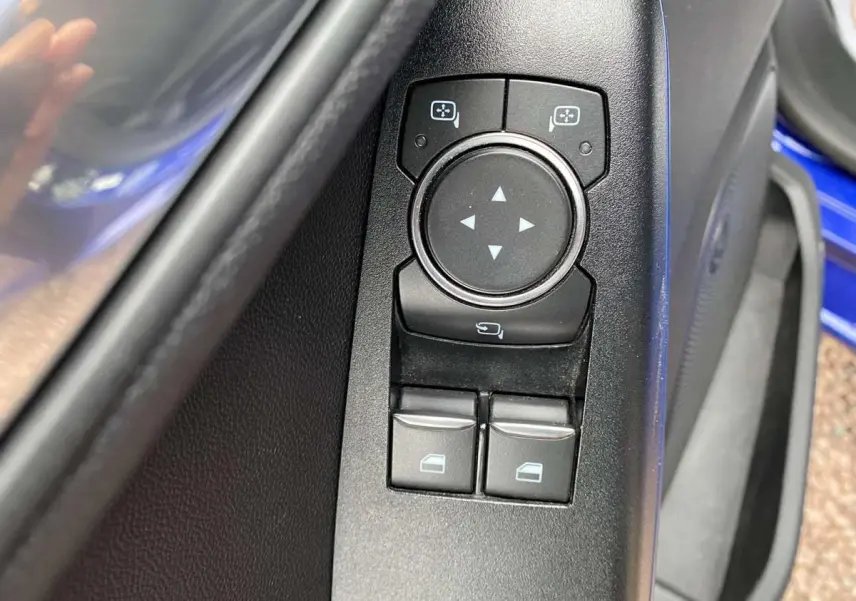 Gros plan sur les commandes de réglage des rétroviseurs et des vitres côté conducteur d'une Ford Fiesta bleu foncé 2017.