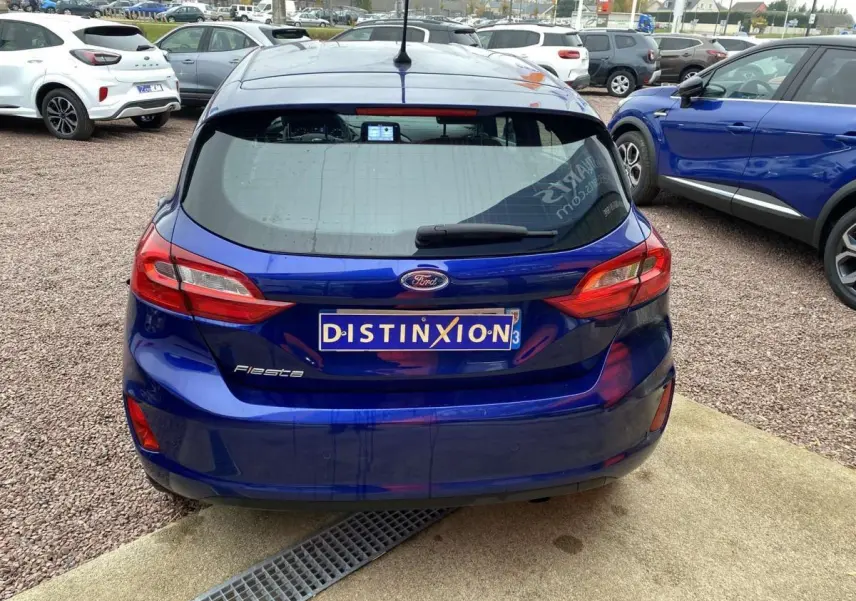 Vue arrière d'une Ford Fiesta bleu foncé 2017 avec plaque Distinxion, stationnée sur sol gravillonné.