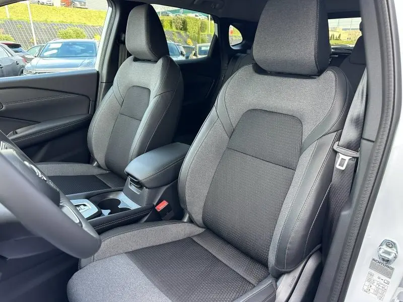 Vue intérieure côté conducteur du Nissan Qashqai Hybrid e-POWER 2025, sièges tissu gris avec surpiqûres et accoudoir central.