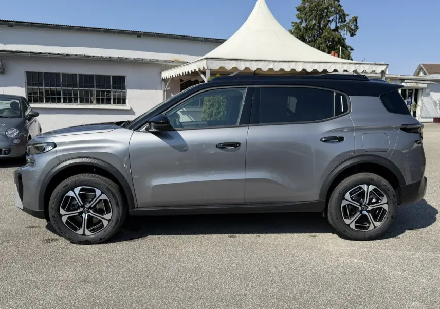 Vue de profil côté gauche d'un Citroën C3 Aircross gris clair avec toit noir et jantes distinctives.