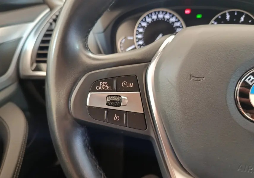 Gros plan sur le volant cuir et alu multifonctions du BMW X3 xDrive20d 2020, boutons de régulateur de vitesse visibles.