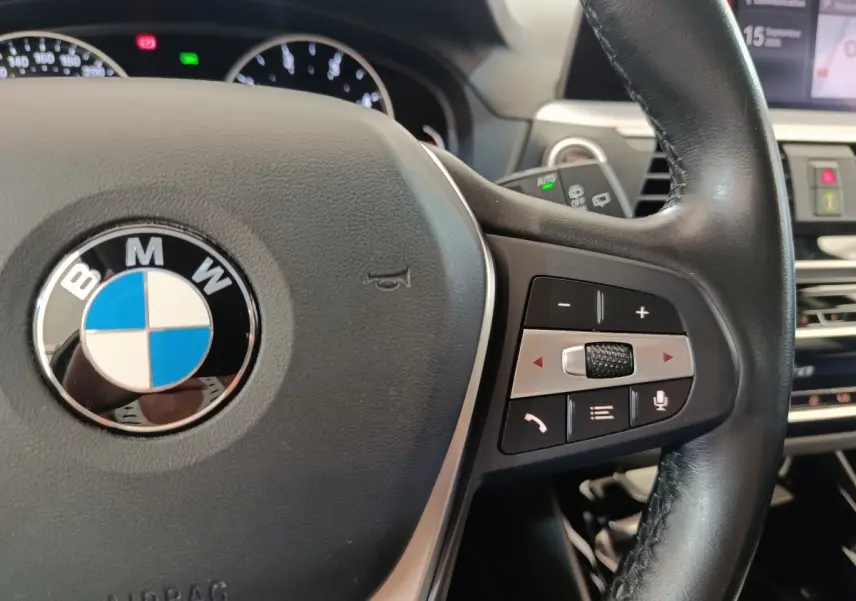 Gros plan sur le volant cuir et alu multifonctions du BMW X3 gris clair, avec commandes intégrées visibles.