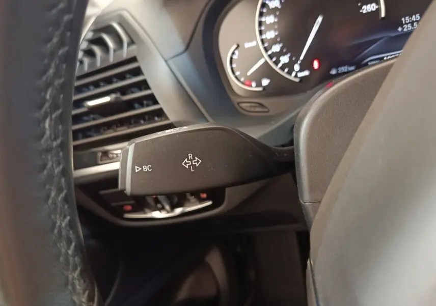 Gros plan sur la manette de clignotant à gauche du volant cuir d’une BMW X3 gris clair, tableau de bord en arrière-plan.