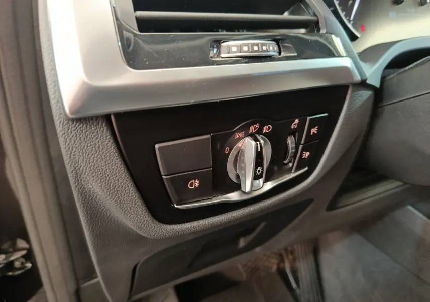 Gros plan sur le panneau de commande des phares à gauche du volant dans l'habitacle gris foncé d'un BMW X3 gris clair.