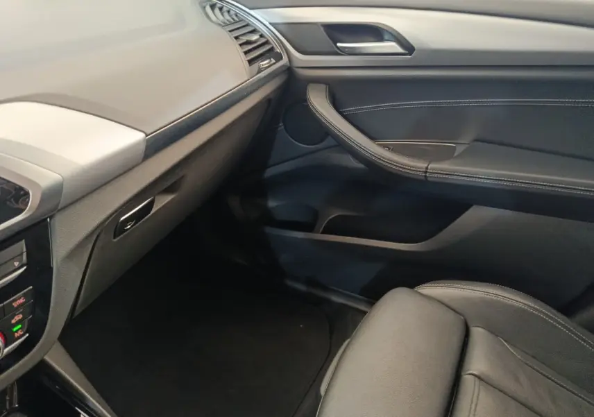 Intérieur côté passager du BMW X3 gris clair 2020, montrant tableau de bord et porte en cuir noir avec surpiqûres.