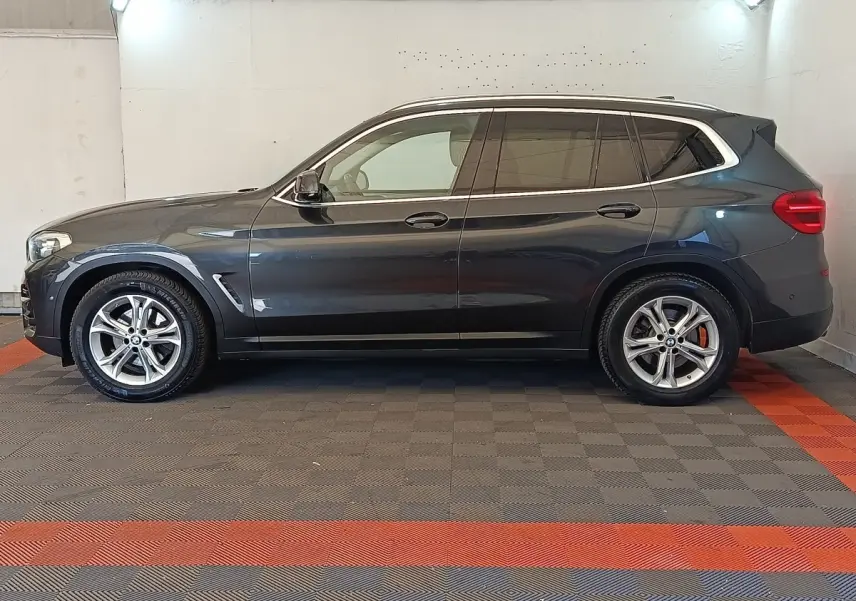Profil côté gauche d'un BMW X3 gris clair 2020 avec jantes alliage et vitres teintées dans un garage.
