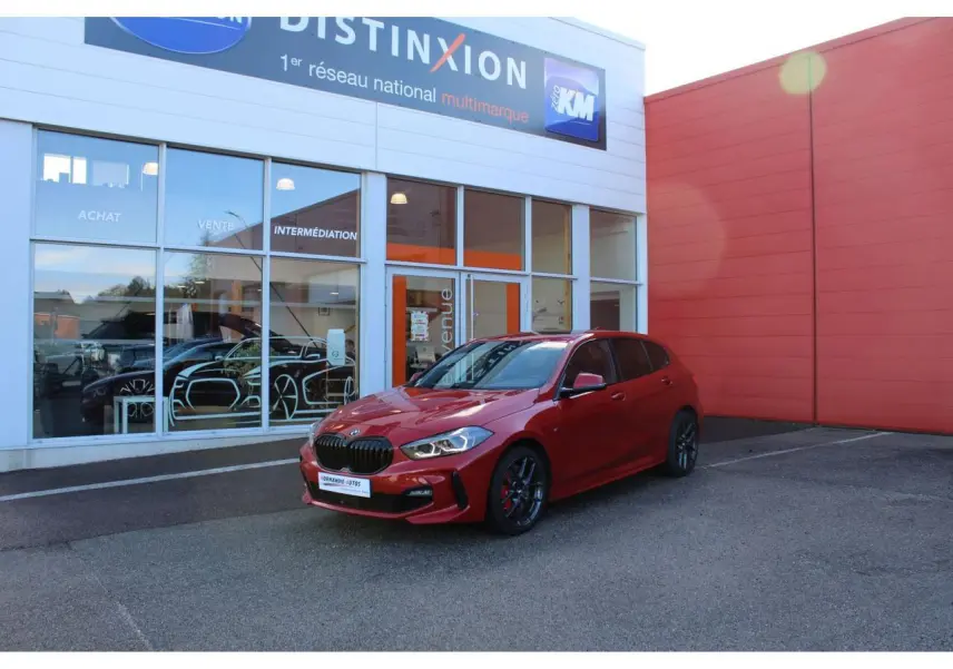 BMW Série 1 118d rouge Melbourne métallisé vue 3/4 avant droit, avec jantes alliage et becquet arrière M Sport.
