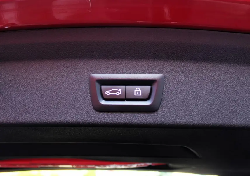 Gros plan sur les boutons d'ouverture et de verrouillage du coffre sur le hayon rouge métallisé d'une BMW Série 1 118d Edition M Sport Pro.