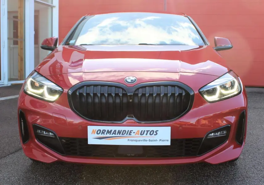 Vue avant d'une BMW Série 1 118d rouge Melbourne avec calandre noire et feux LED allumés.