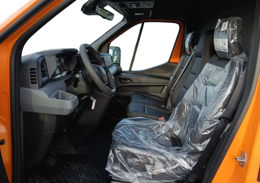 Vue intérieure côté conducteur du Renault Master orange 2026, montrant le volant, tableau de bord et sièges protégés par film plastique.