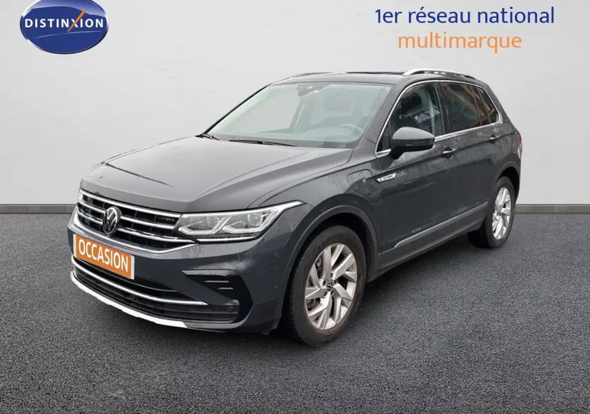 Volkswagen Tiguan 1.4 E-Hybrid gris lunaire en 3/4 avant droit sur sol gris devant un mur blanc.