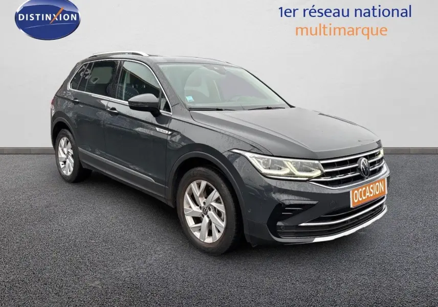 Volkswagen Tiguan 1.4 E-Hybrid gris lunaire vu en 3/4 avant droit avec phares LED allumés sur fond neutre.