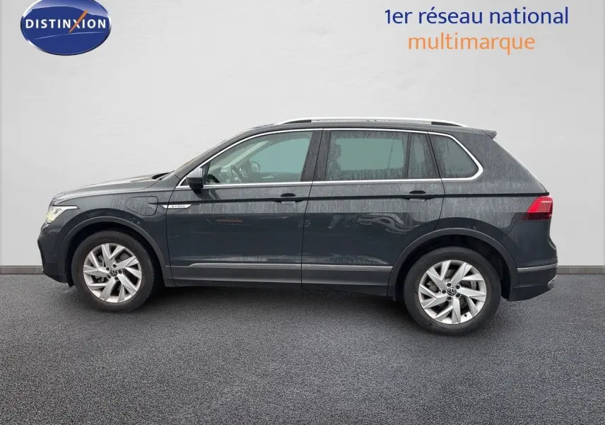 Profil côté gauche d'un Volkswagen Tiguan 1.4 e-Hybrid gris lunaire, avec jantes alliage et toit ouvrant visible.