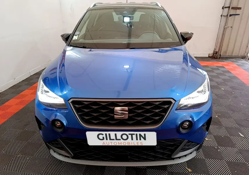 Vue avant d'une SEAT Arona bleu vif avec phares LED allumés dans un garage fermé.