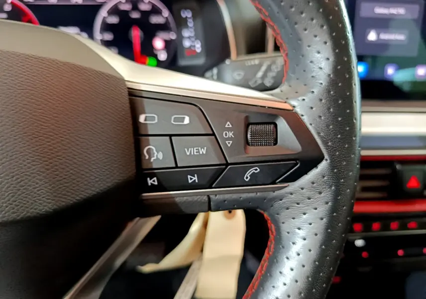 Gros plan sur la partie droite du volant en cuir perforé avec surpiqûres rouges du SEAT Arona 2022, boutons multifonctions visibles.
