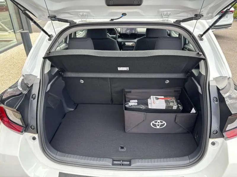 Coffre ouvert d'une Toyota Yaris 116h Dynamic blanche vue arrière, avec un organiseur Toyota contenant des accessoires.