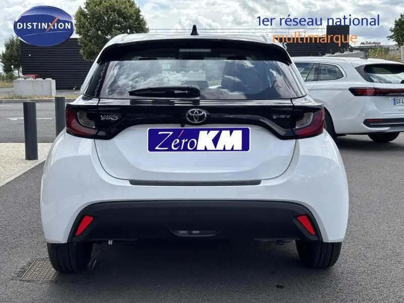 Vue arrière d'une Toyota Yaris 116h Dynamic blanche 2025 avec toit noir et feux arrière foncés, en stationnement extérieur.