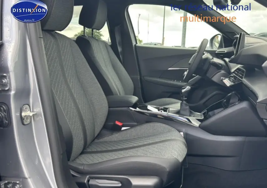 Vue intérieure côté conducteur du Peugeot 2008 gris artense, mettant en valeur les sièges en tissu et la boîte manuelle.