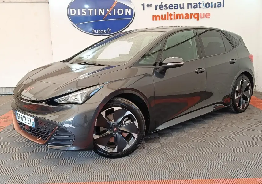 Vue 3/4 avant droite d'une CUPRA BORN gris foncé avec jantes noires et détails cuivrés, stationnée en intérieur showroom.