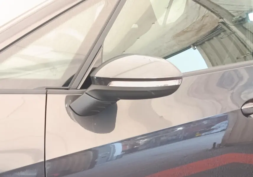 Gros plan sur le rétroviseur côté gauche d'une CUPRA BORN gris foncé, avec reflet sur la portière.