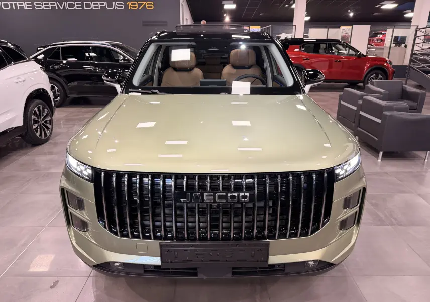 Vue avant du SUV hybride rechargeable JAECOO J7 gris olive, avec calandre verticale noire et intérieur cuir brun visible.