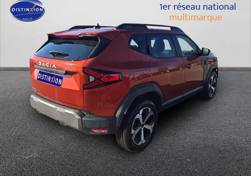 Vue 3/4 arrière droite du Dacia Duster 2025 brun terracotta avec barres de toit et jantes alu distinctives.