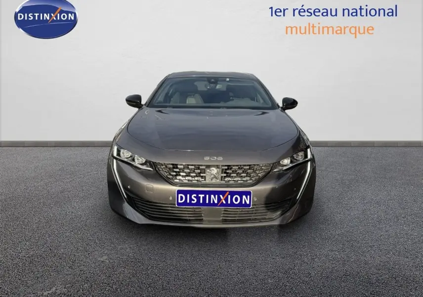 Vue de face d'une Peugeot 508 gris platinium 2023 stationnée sur un parking de concession multimarque.