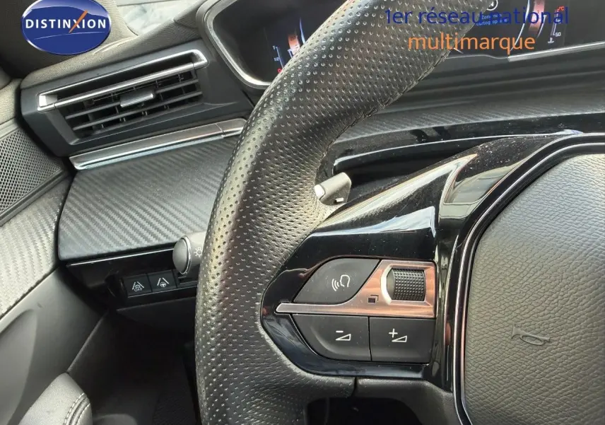 Gros plan sur le volant en cuir perforé côté gauche du Peugeot 508 gris platinium, avec commandes intégrées et tableau de bord partiel.