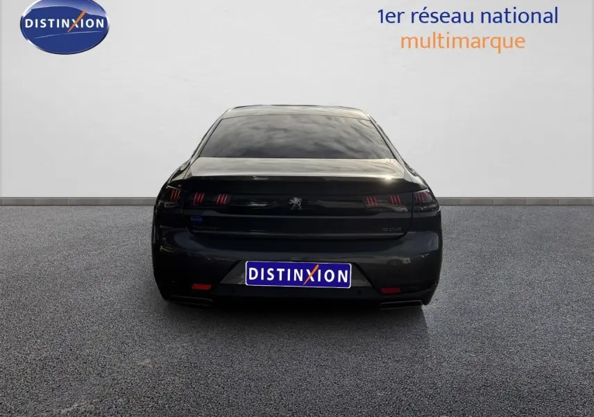 Vue arrière d'une Peugeot 508 gris platinium 2023 stationnée en extérieur sous un ciel partiellement nuageux.