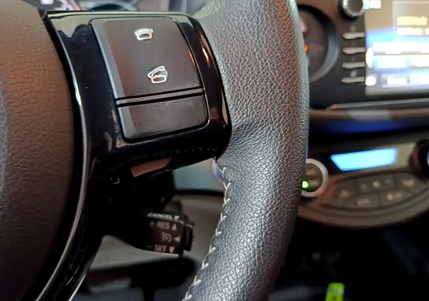 Gros plan sur le volant cuir noir de la Toyota Yaris hybride 2020 avec commandes intégrées et tableau de bord flou en arrière-plan.