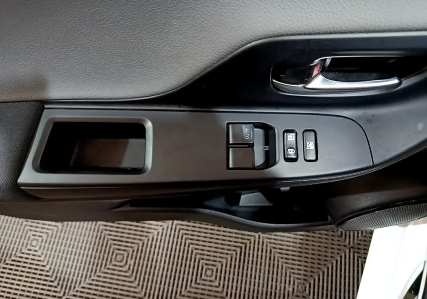 Détail de la porte intérieure côté conducteur de la Toyota Yaris blanche, montrant les commandes des vitres et la poignée chromée.