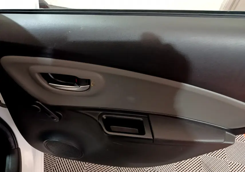 Vue intérieure côté gauche de la porte avant d'une Toyota Yaris blanche, avec poignée chromée et panneau noir et gris.