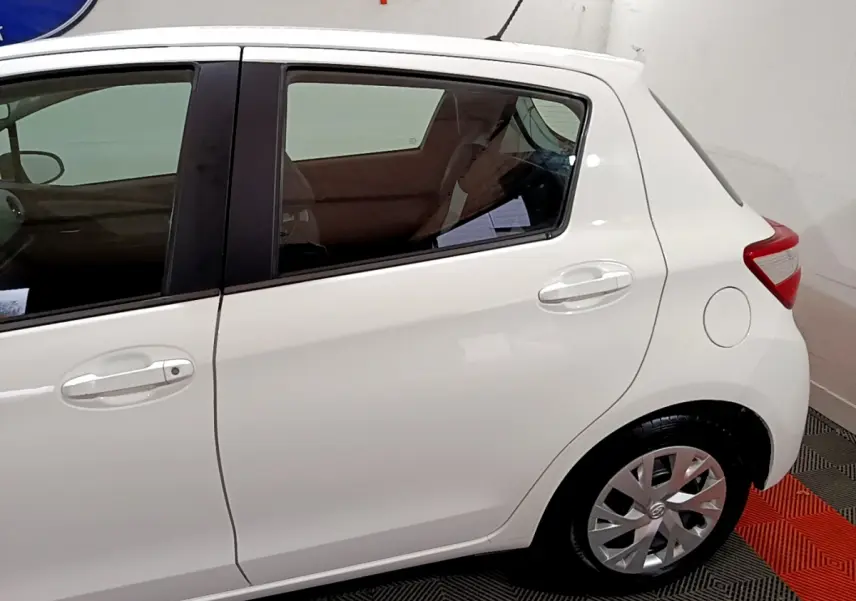 Vue latérale côté droit de la Toyota Yaris blanche 1.5 Hybride 2020, mettant en valeur la porte arrière et la roue arrière.