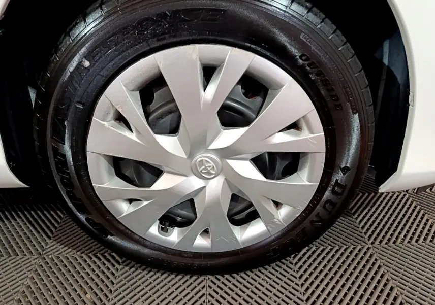 Gros plan sur la roue avant droite d'une Toyota Yaris blanche, jante avec enjoliveur argenté et pneu Dunlop.