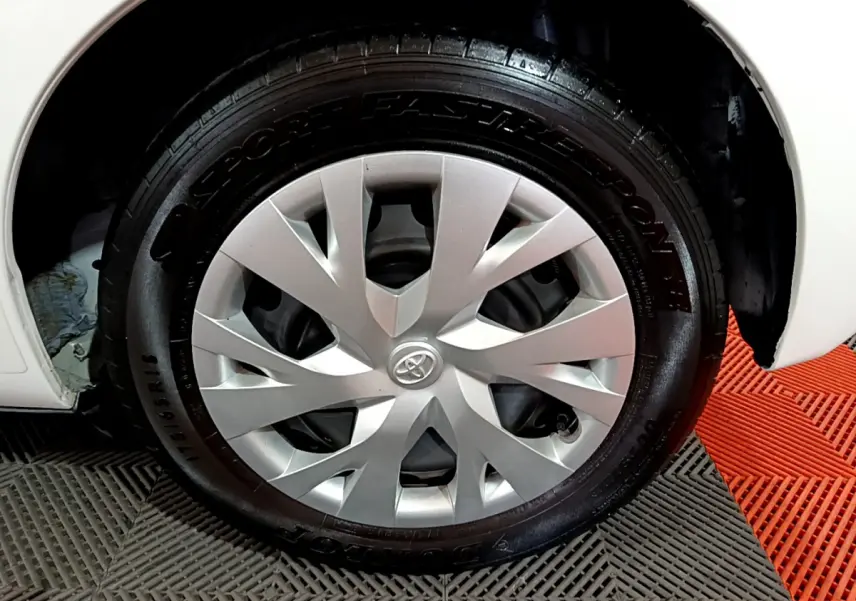 Gros plan sur la roue avant droite d'une Toyota Yaris blanche, avec enjoliveur argenté et pneu Dunlop.