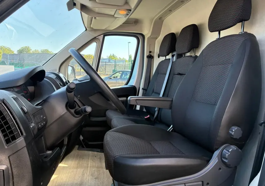 Vue intérieure côté conducteur du Peugeot Boxer cabine approfondie 2019, sièges noirs en tissu avec accoudoir central.