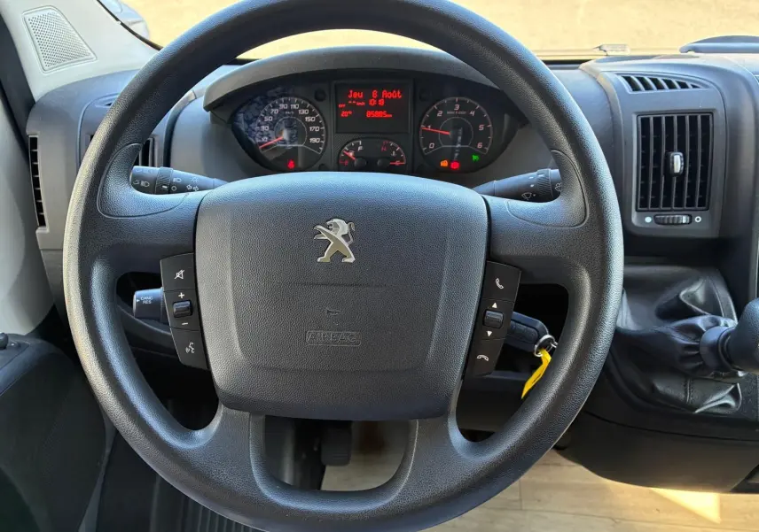 Vue rapprochée du volant noir de la Peugeot Boxer 2.2 BlueHDi 165 2019 avec tableau de bord et levier de vitesses manuel.