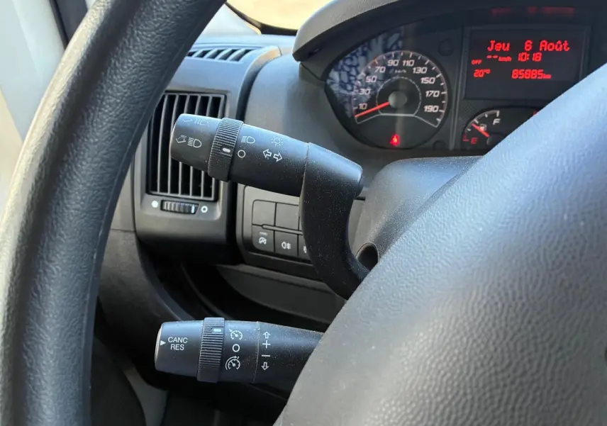 Gros plan sur le volant et les commandes du tableau de bord du Peugeot Boxer cabine approfondie gris, avec compteur et affichage digital rouge.