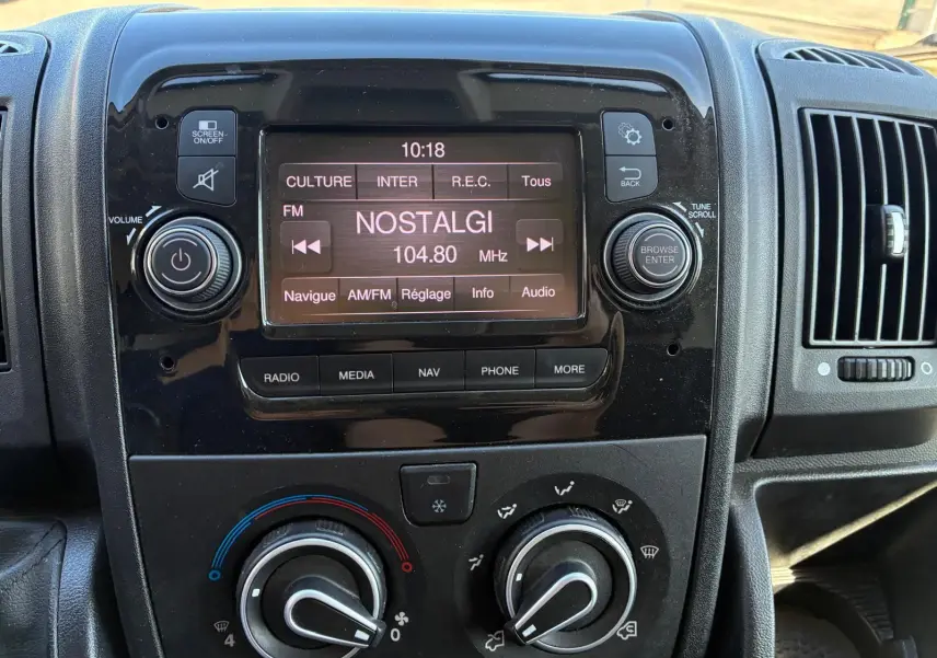 Vue rapprochée du tableau de bord noir du Peugeot Boxer Cabine Approfondie 2019 avec écran radio affichant la station Nostalgie.